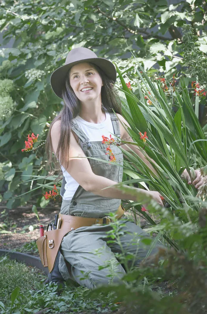 The designer kneeling at work in a planted bed, looking up and smiling