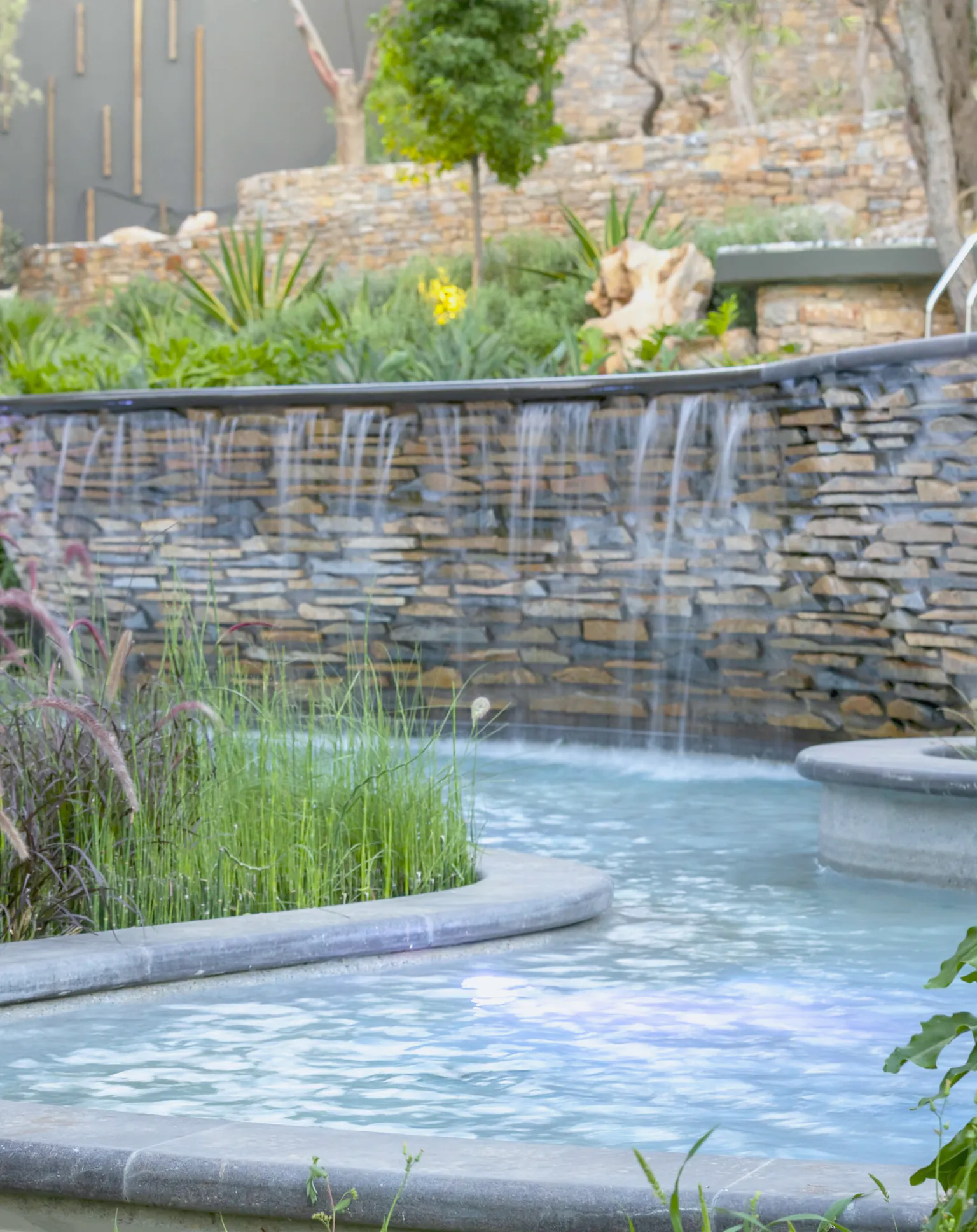A stone water wall beside horsetail and ferns
