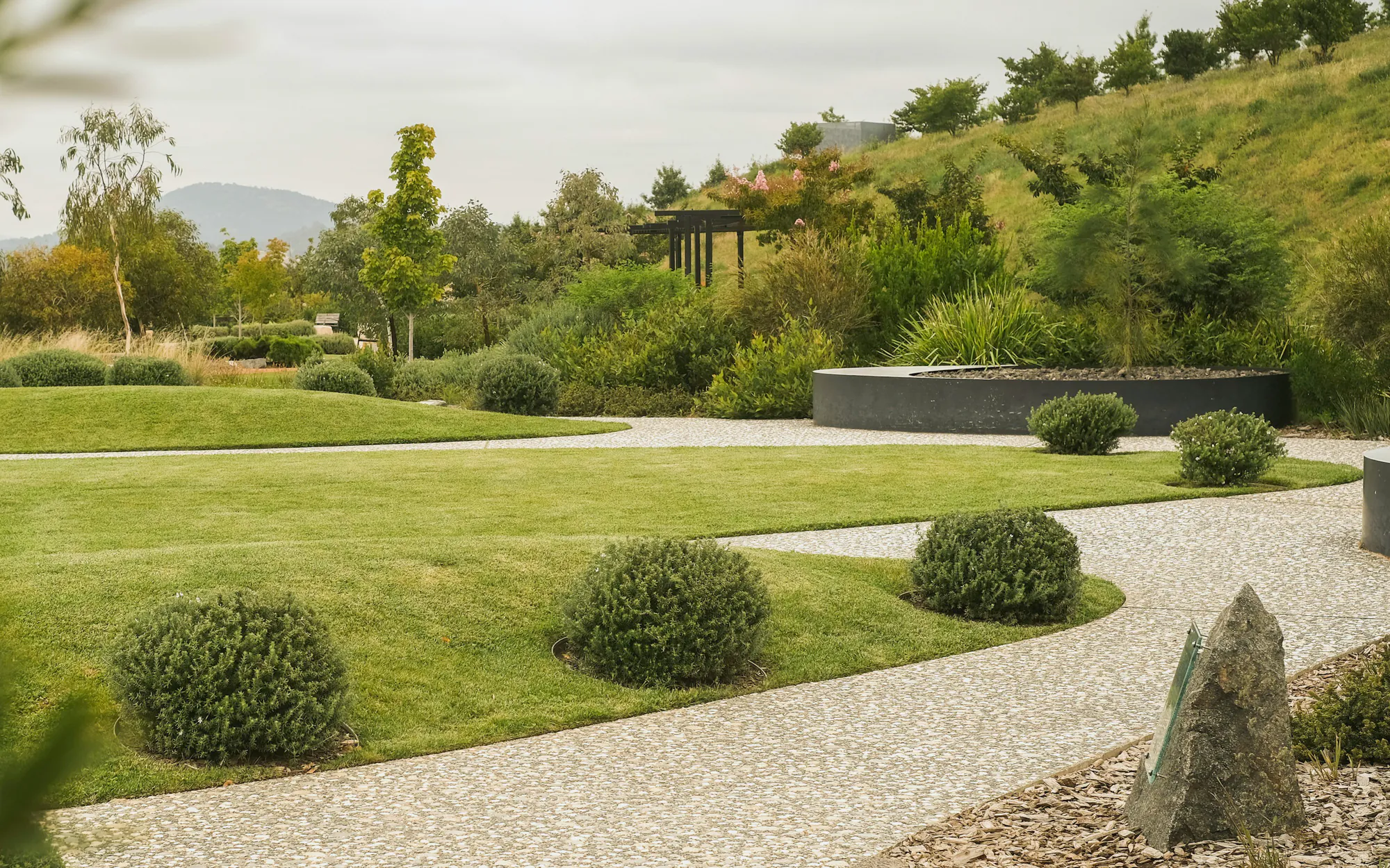 A curved lawn, a gravel path and clipped shrubs below a grassy slope